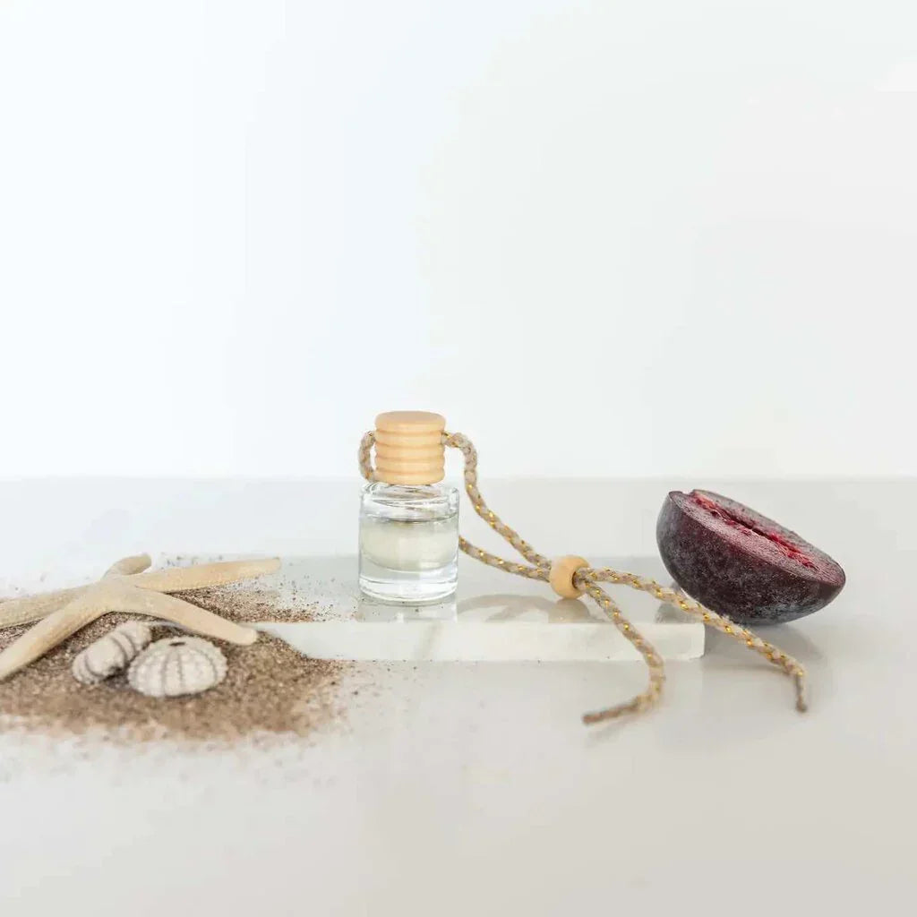 Car diffuser with wooden top, next to a dark plum, beach sand, starfish, seashells for women’s boho chic clothing shop Daisy