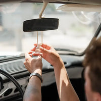 Clear glass car diffuser with wooden top hanging from rearview mirror for freshening car interior