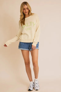 Cream-colored Salty Vibes light weight sweater paired with denim shorts and white sneakers