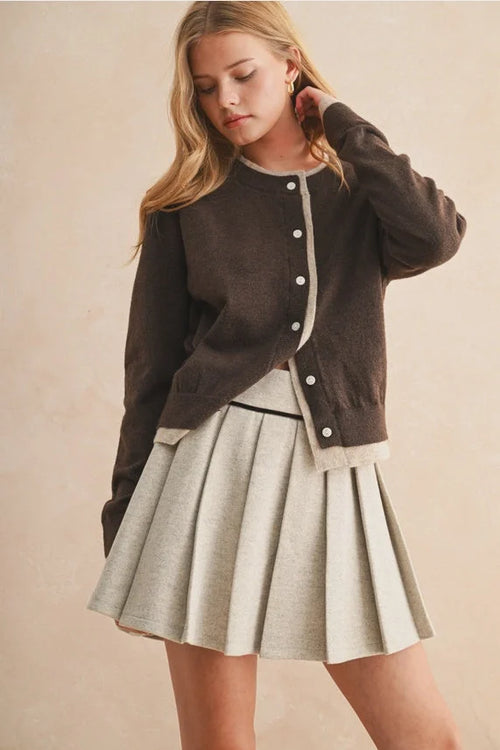 Long-sleeved dark brown cardigan with white contrast buttons and cream trim over a cream mini skirt