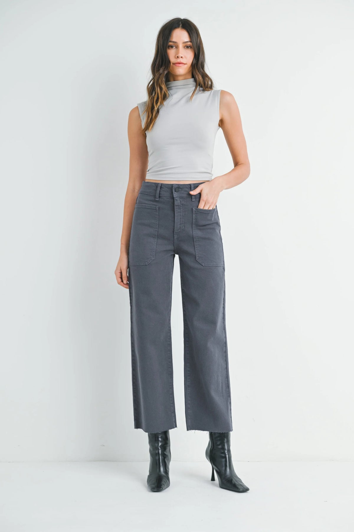 Model wearing light grey sleeveless mock neck top and dark grey wide leg denim pants with black heeled ankle boots