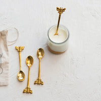 Golden brass spoons with bee design in printed drawstring bag, one spoon in creamy substance