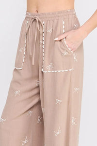 Taupe embroidered linen pants with bow pattern and scallop trim for a stylish look