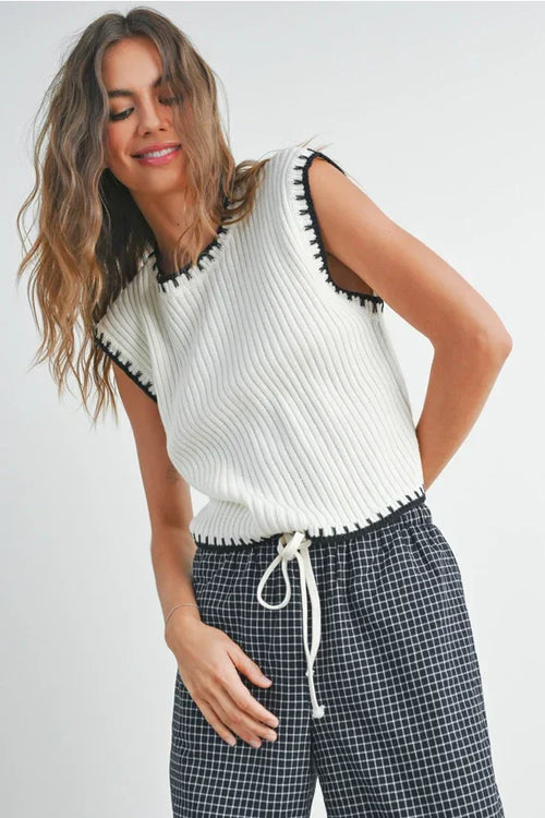 White ribbed knit sleeveless sweater vest with black whipstitch trim and drawstring hem