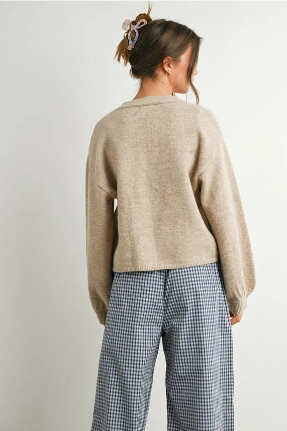 Woman wearing beige long sleeve cardigan with neck cuff button-up design and checkered pants