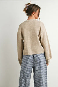 Woman wearing beige long sleeve cardigan with neck cuff button-up design and checkered pants