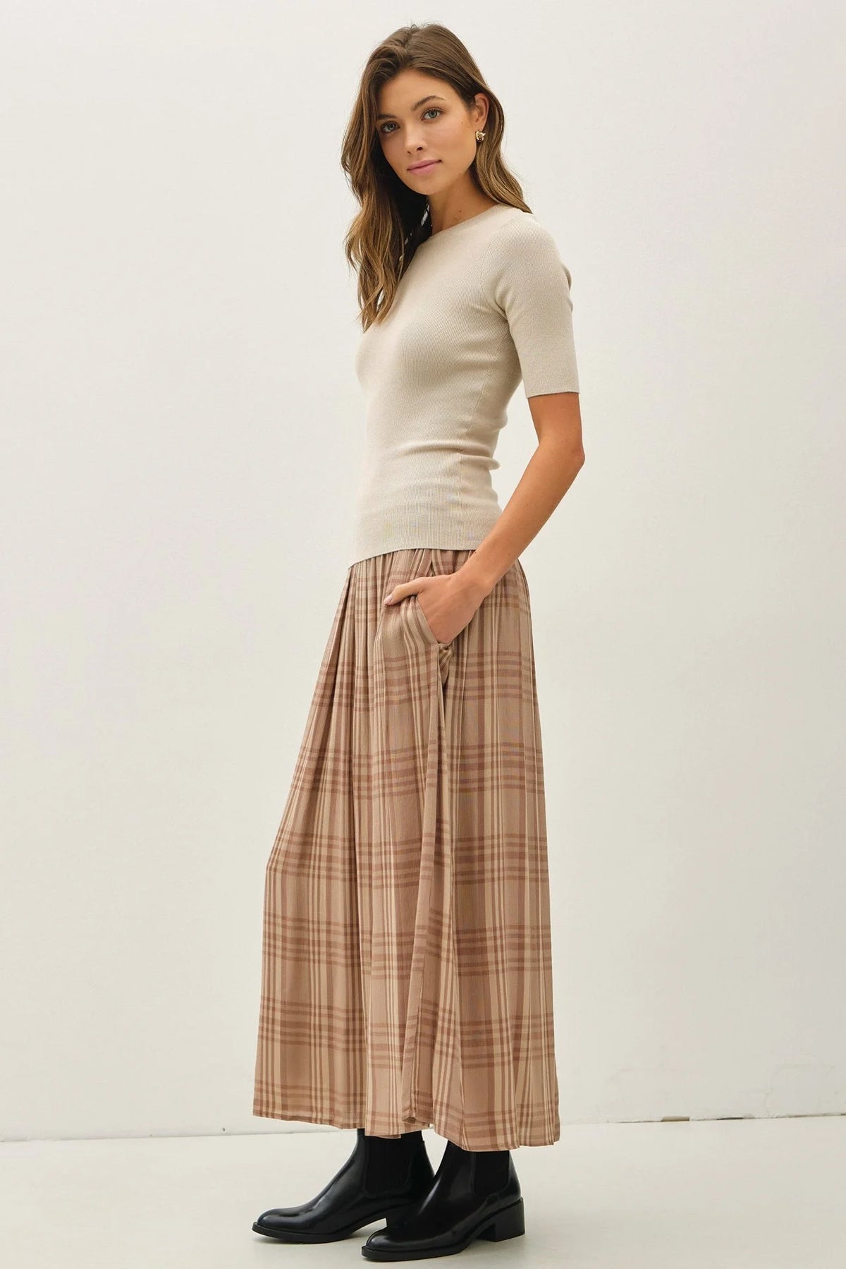 Woman wearing beige ribbed top and plaid printed pleats midi skirt with black ankle boots