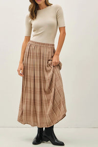 Woman wearing beige top and plaid printed pleats midi skirt with black ankle boots
