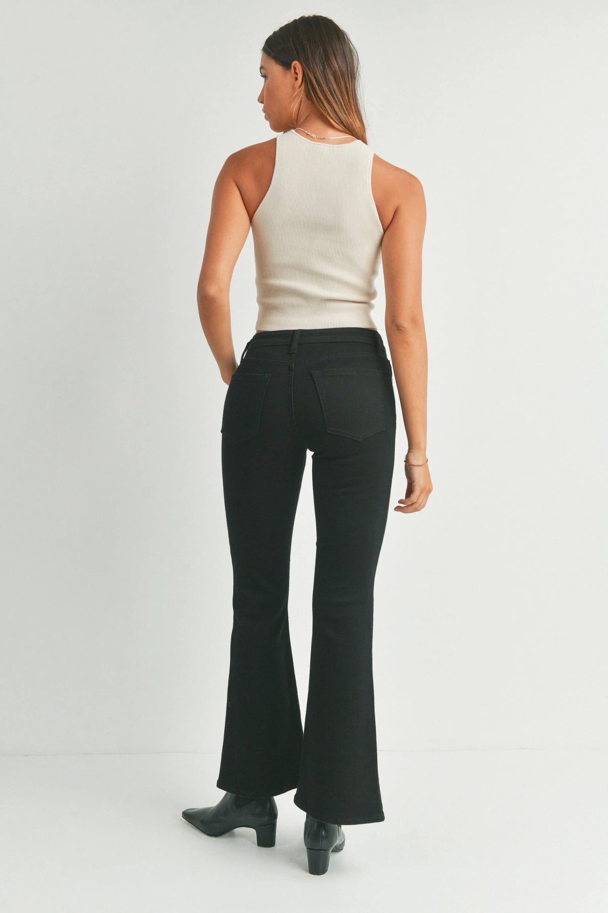 Woman modeling beige sleeveless ribbed knit top with low rise flare denim jeans