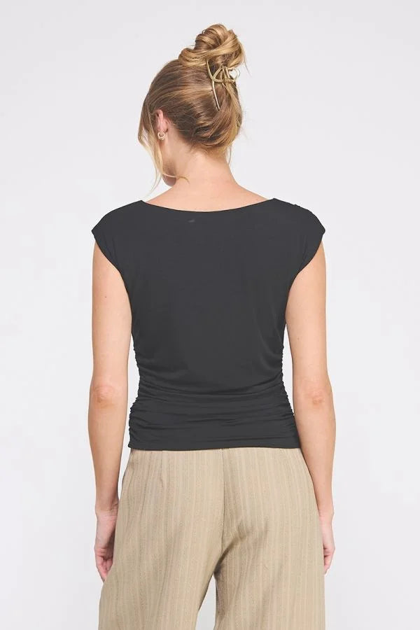 Woman wearing a black sleeveless boat neck scrunch tank top and beige pleated pants