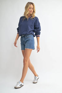 Woman in blue sweatshirt and denim walking shorts showcasing longer length denim walking shorts