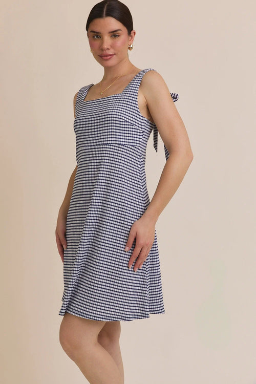 Woman wearing a blue and white gingham stripe sleeveless mini dress with shoulder ties