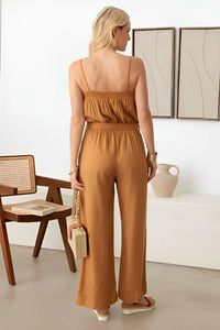 Woman in caramel sleeveless jumpsuit with flowy wide-leg pants and smocked neck line