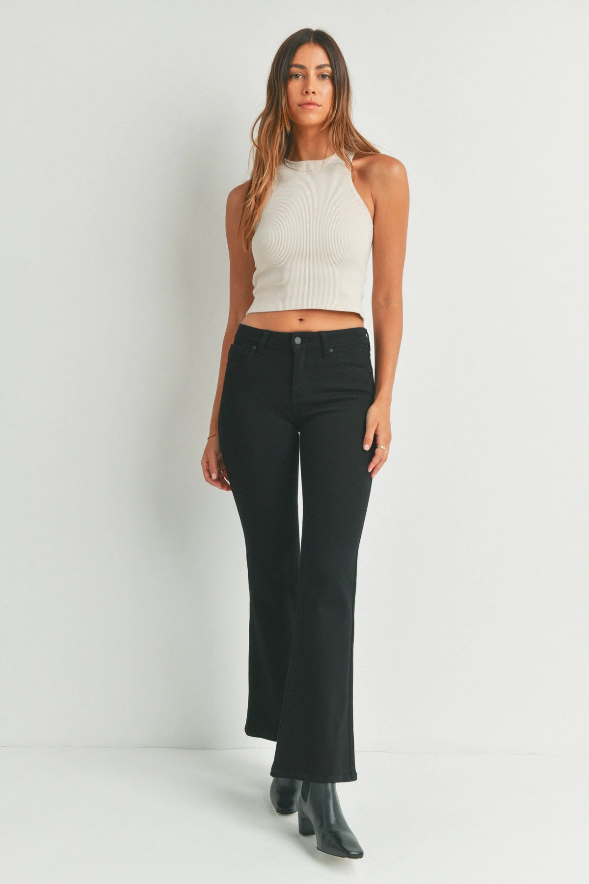 Woman wearing low rise flare denim jeans with cream halter crop top and black heeled boots