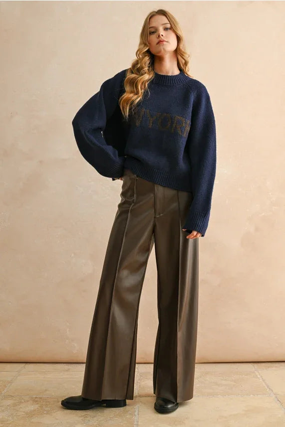 Woman wearing NEW YORK LETTER FRONT SWEATER and wide-leg faux leather trousers in women’s boho chic clothing style