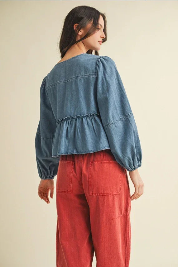 Woman wearing a denim peplum top with ruffle hem and tie closure, paired with red wide-leg pants