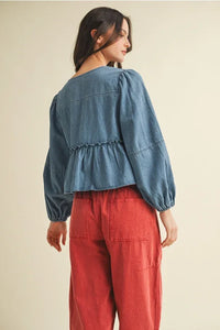 Woman wearing a denim peplum top with ruffle hem and tie closure, paired with red wide-leg pants