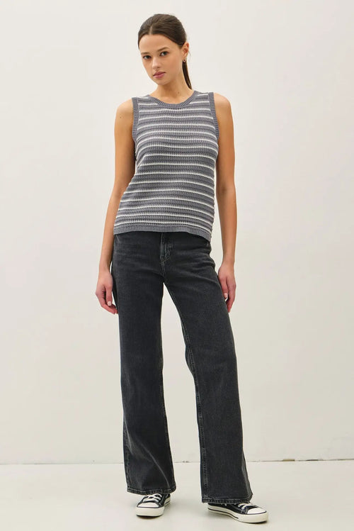 Woman wearing a gray and white striped sweater tank top paired with black jeans