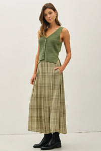 Woman wearing plaid printed pleats midi skirt with green sleeveless top and black boots