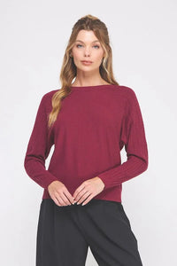 Woman wearing a deep red fine gauge boat neck sweater and black trousers