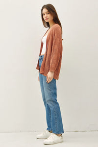 Woman wearing a rust-colored crochet knit cardigan with jeans and white sneakers