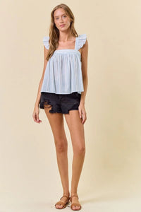 Woman in striped ruffle cap top and distressed denim shorts, perfect for women’s boho chic clothing at Shop Daisy