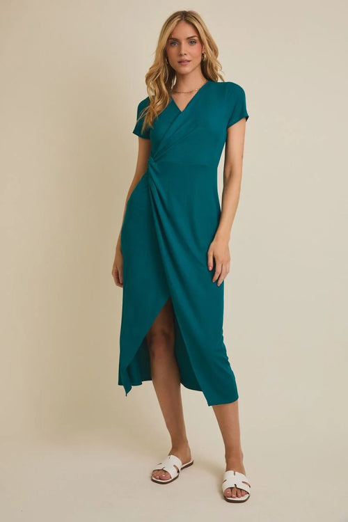 Woman wearing teal short sleeve surplice midi dress with twist detail and white slide sandals