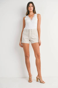 Woman in a white top and beige shorts showcasing the high rise patch pocket denim short