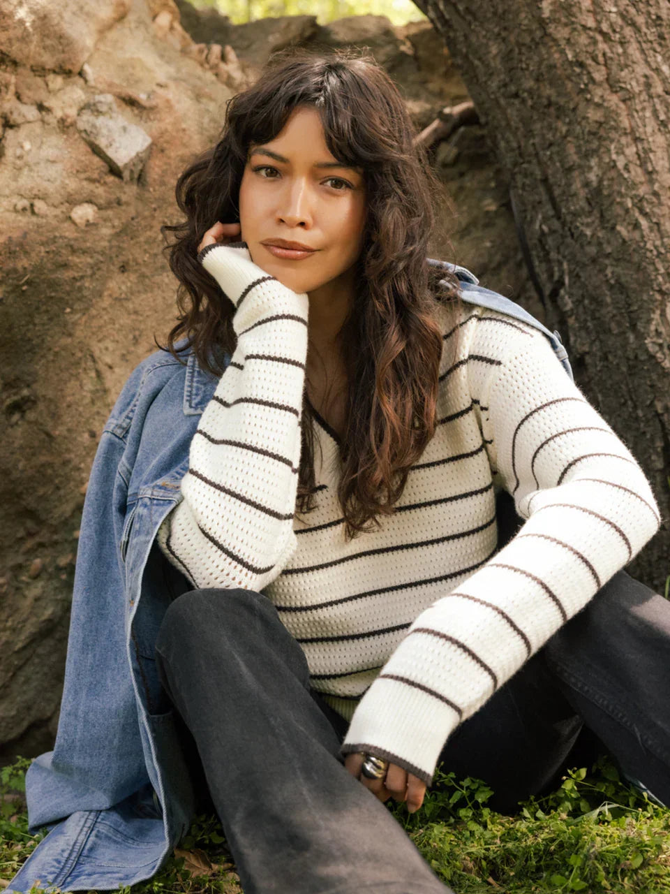 Woman wearing a white and black striped IRA Sweater with black pants and denim jacket