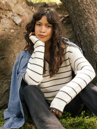 Woman wearing a white and black striped IRA Sweater with black pants and denim jacket