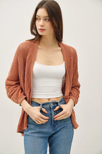 Woman wearing a white tank top and blue jeans with a rust-colored crochet knit cardigan