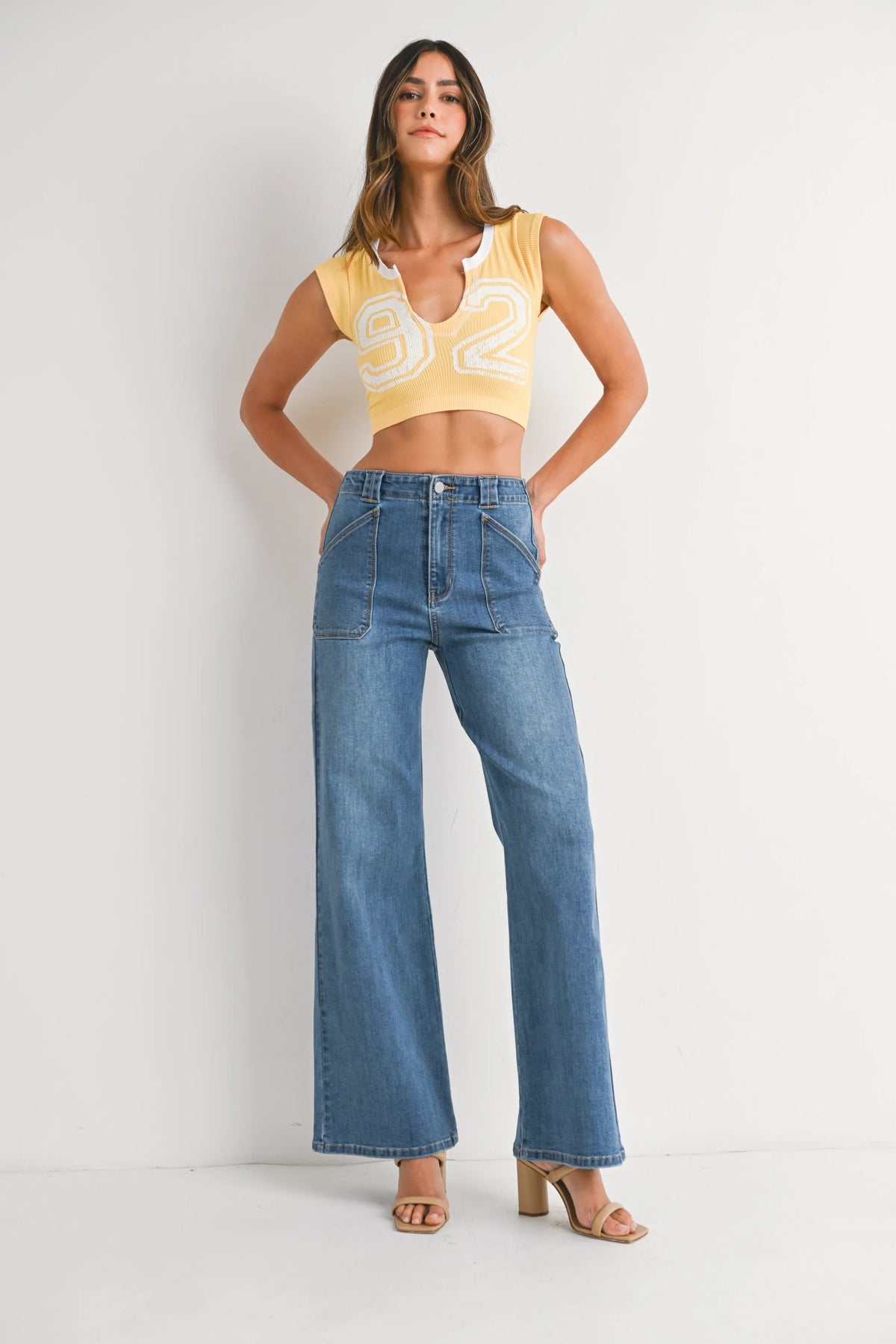 Woman modeling yellow crop top and patch pocket wide leg flare denim jeans with light brown heels