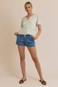 Woman wearing floral embroidered pleated denim shorts and a floral blouse outfit