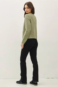 Woman wearing a light-green chunky knit open front cardigan with black flared trousers