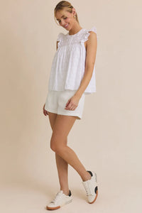 Woman wearing a white round neck ruffle sleeve button down top and shorts outfit