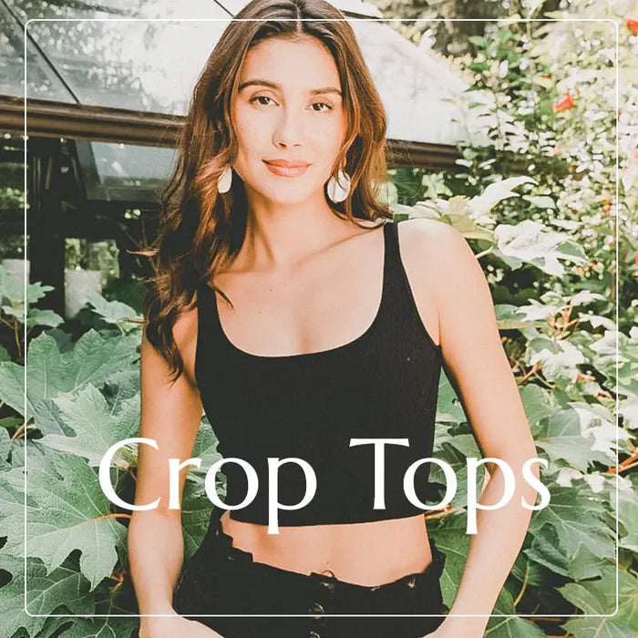 Woman in a black crop top with a leafy background in a boho style setting.