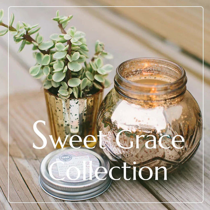 Lit Sweet Grace candle in glass jar beside small potted plant in Grace Candle Collection.