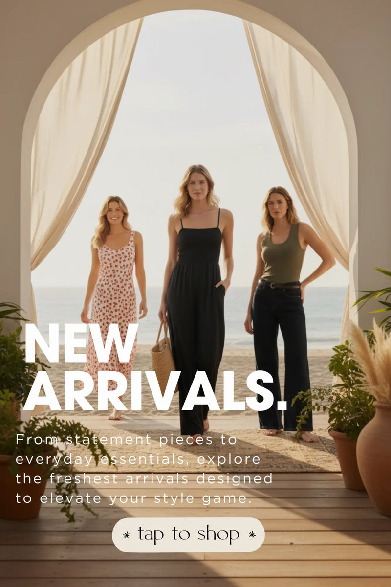 Three women stand under an arched doorway, dressed in stylish outfits including a floral dress, a black jumpsuit, and dark pants.