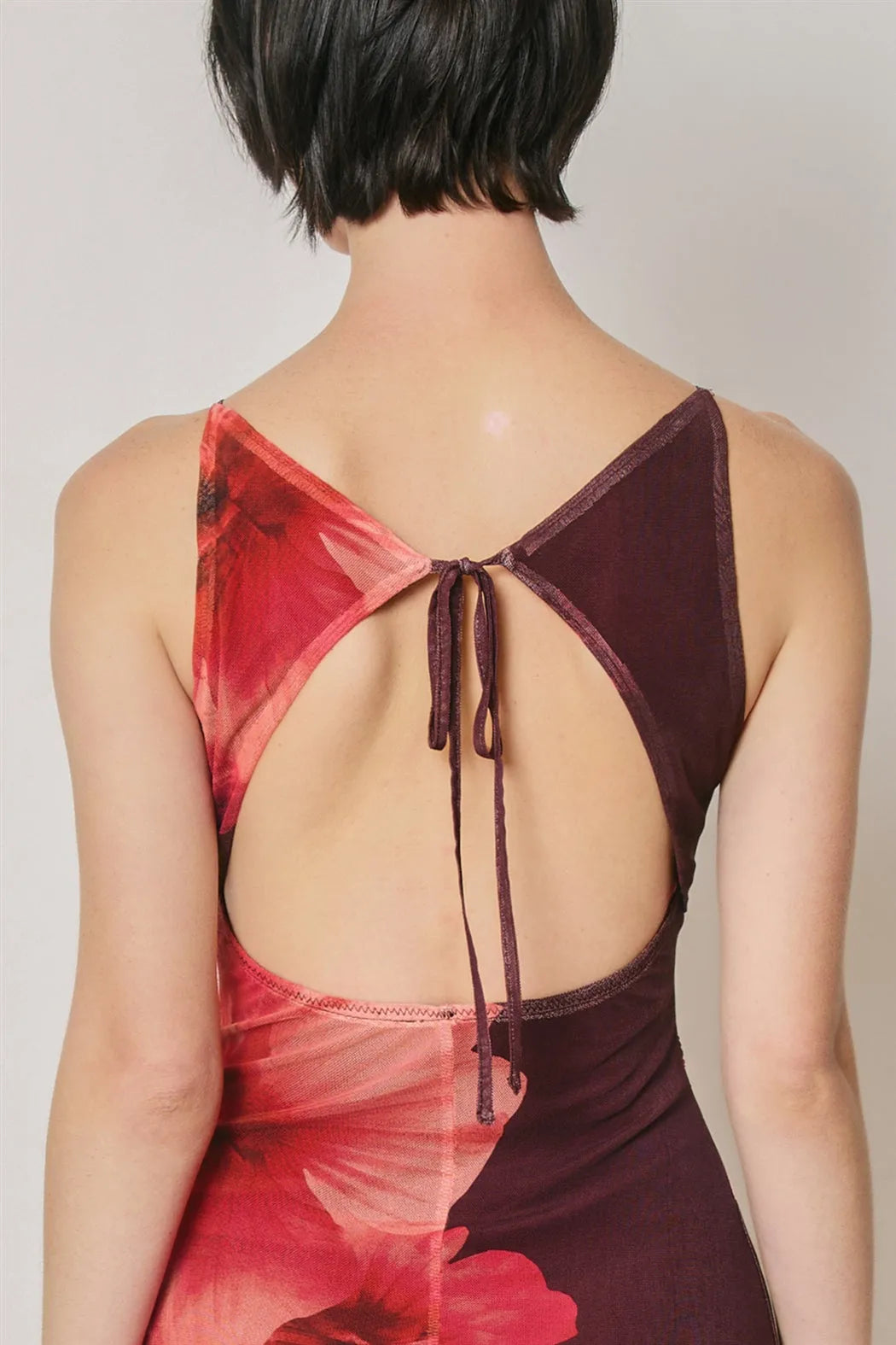 Back view of a floral mesh open back maxi dress in vibrant red and burgundy with sheer panels and adjustable tie straps