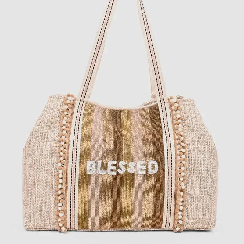 Beige and gold striped woven tote bag with pom-pom trim and white blessed embroidery for women’s boho chic clothing