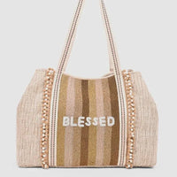 Beige and gold striped woven tote bag with pom-pom trim and white blessed embroidery for women’s boho chic clothing