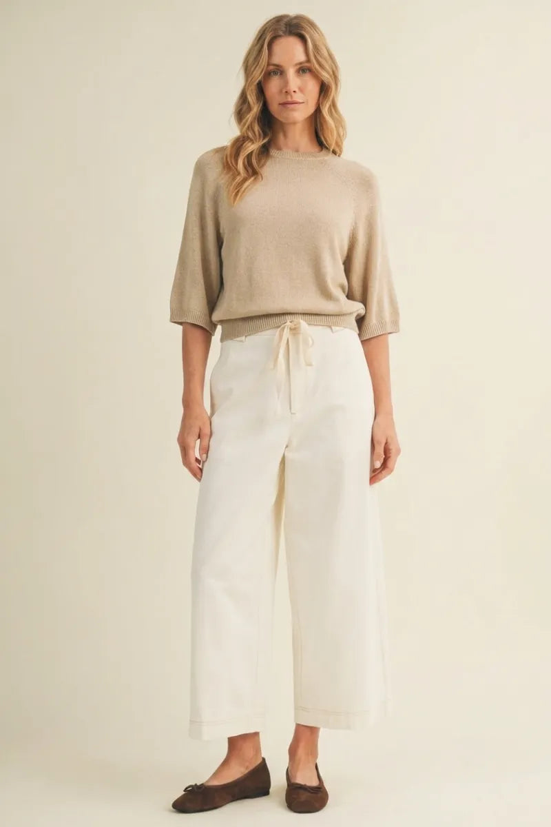 Beige knit sweater with three-quarter sleeves and drawstring waist paired with pull on baggy fit pants