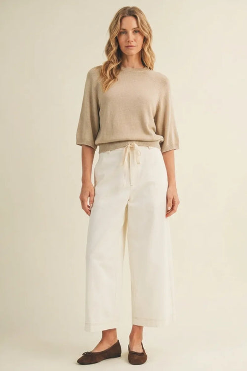 Beige knit sweater with three-quarter sleeves and drawstring waist paired with pull on baggy fit pants
