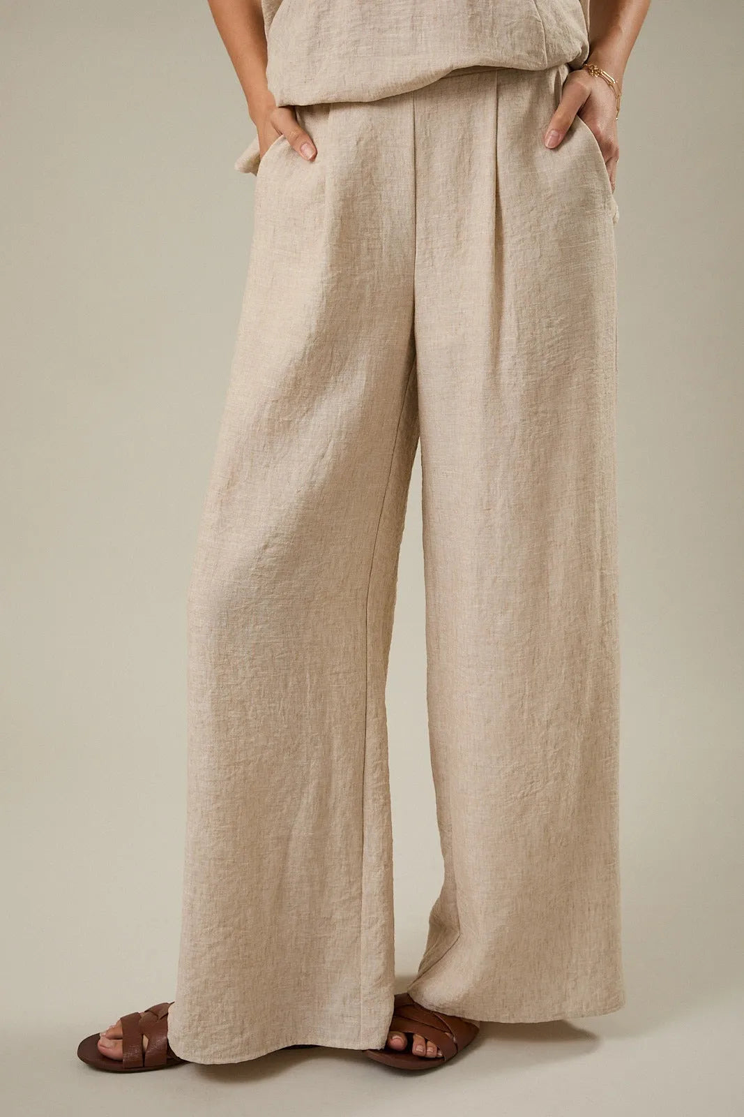 Beige linen wide leg pants with elastic back and front pleat detail featuring a relaxed pleated design