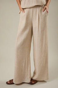 Beige linen wide leg pants with elastic back and front pleat detail featuring a relaxed pleated design