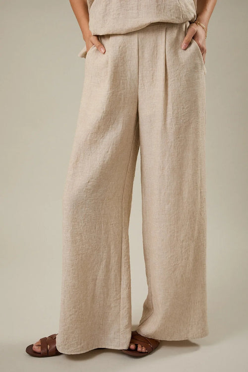 Beige linen wide leg pants with elastic back and front pleat detail featuring a relaxed pleated design