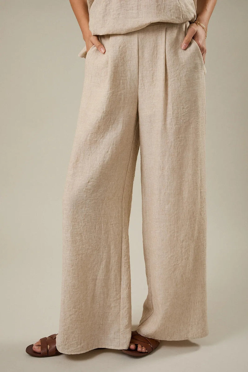 Beige linen wide leg pants with elastic back and front pleat detail featuring a relaxed pleated design