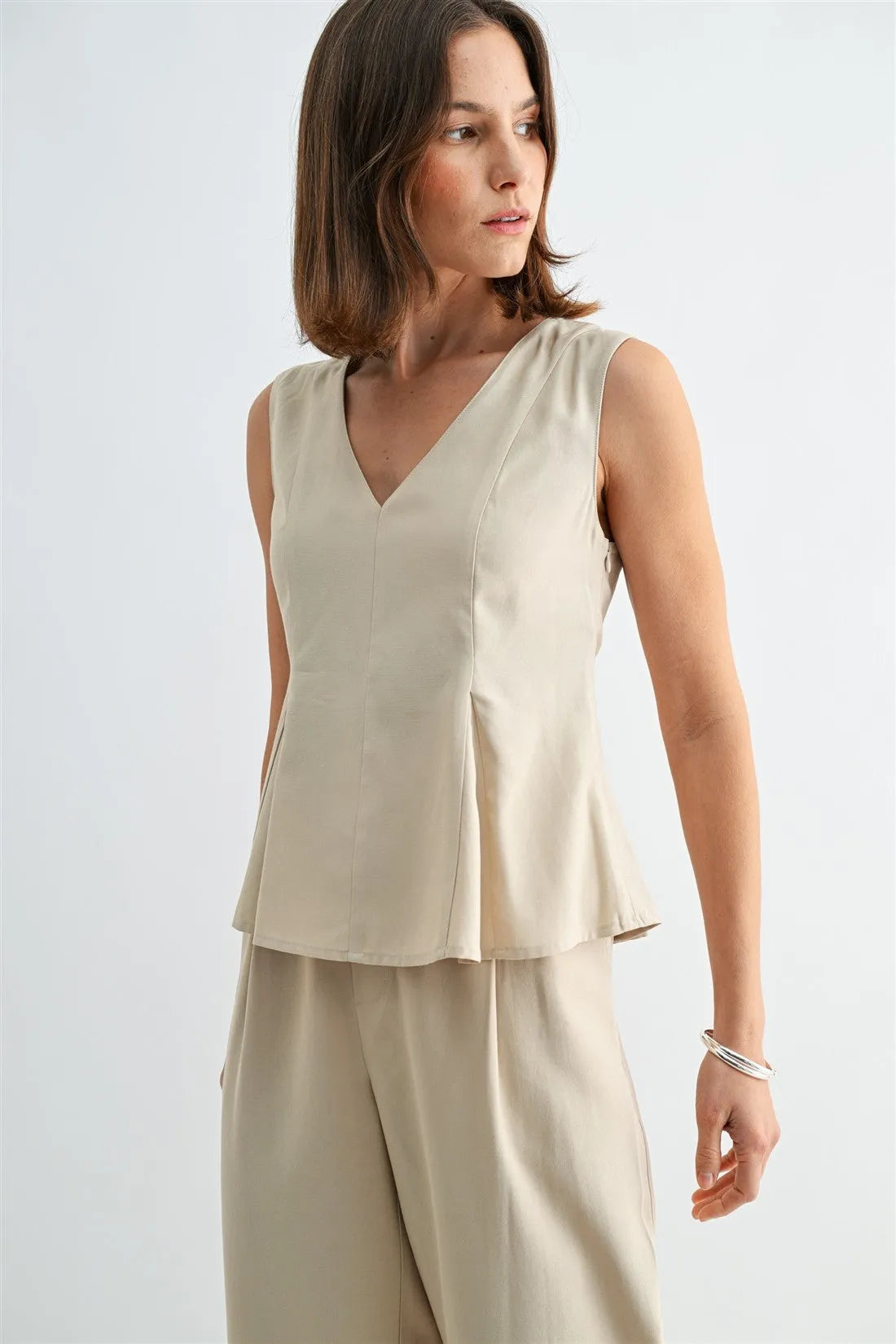 Beige v neck peplum sleeveless blouse with subtle hem pleating and fitted waist for a stylish look
