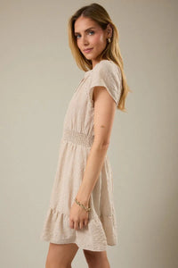 Beige and white vertically striped mini dress with notch neck short sleeve and smocked waistband with ruffled hem