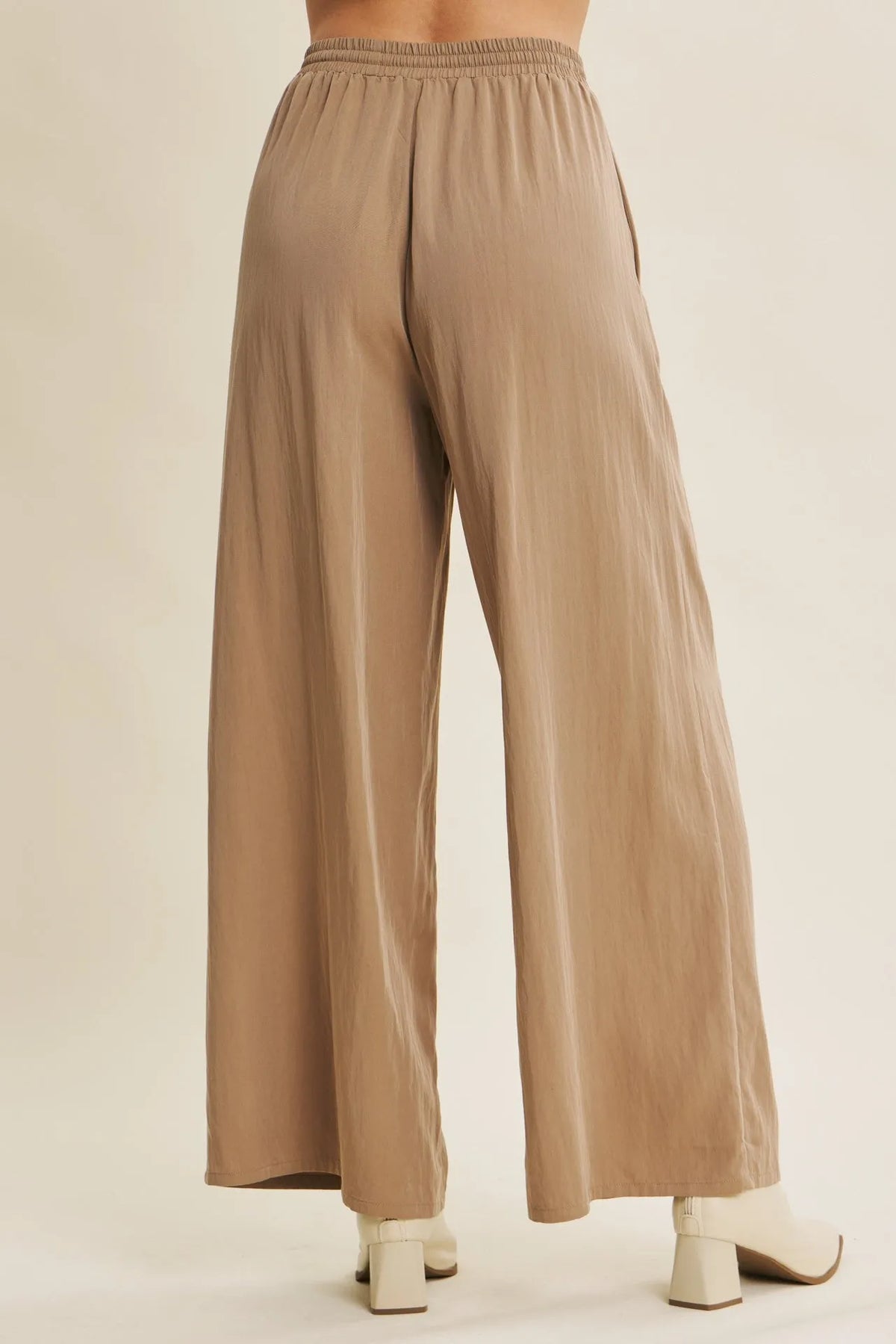 Beige wide leg pants with elastic waistband made from lightweight flowing fabric featuring a step washed look